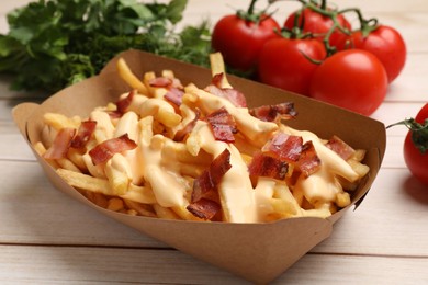 Photo of Tasty potato fries, cheese sauce, bacon and products in paper container on light wooden table, closeup