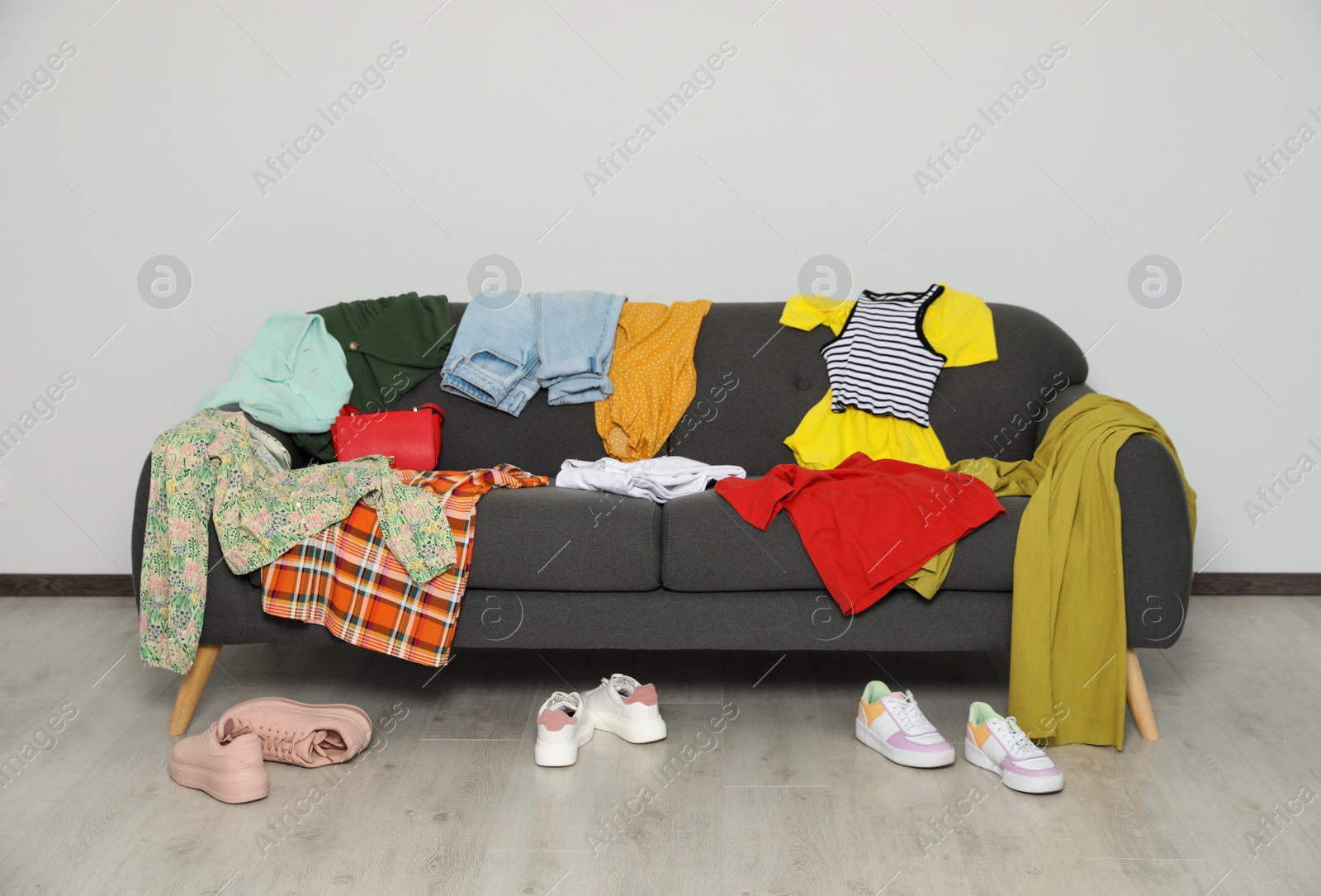 Photo of Messy pile of clothes on sofa and shoes in living room