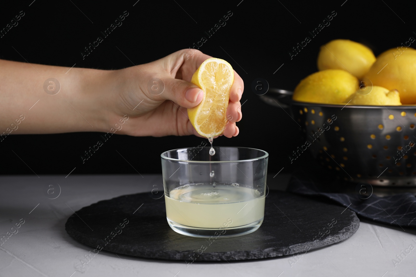 Photo of Woman squeezing lemon juice into glass bowl at grey table, closeup