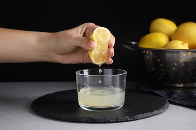 Photo of Woman squeezing lemon juice into glass bowl at grey table, closeup