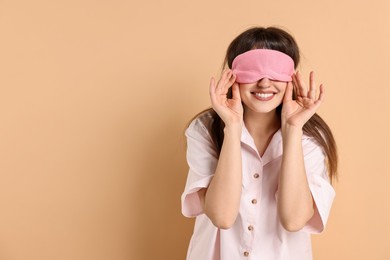 Photo of Woman in pyjama and sleep mask on beige background, space for text