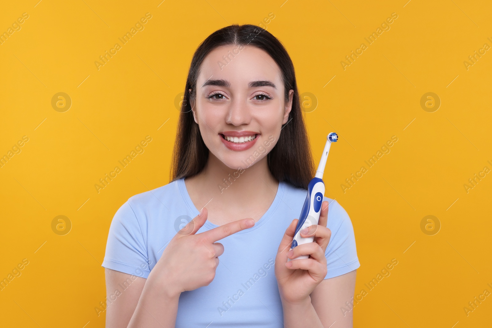 Photo of Happy young woman holding electric toothbrush on yellow background