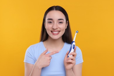 Photo of Happy young woman holding electric toothbrush on yellow background