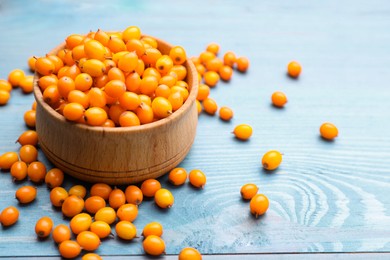 Photo of Bowl with fresh ripe sea buckthorn berries on light blue wooden table, space for text