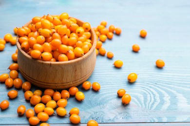 Bowl with fresh ripe sea buckthorn berries on light blue wooden table, space for text