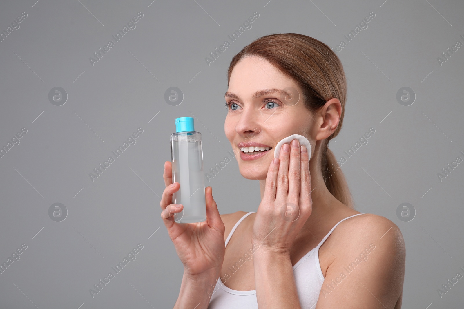 Photo of Beautiful woman removing makeup with cotton pad on gray background, space for text