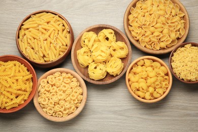 Photo of Different types of pasta on light grey wooden table, flat lay