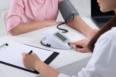 Doctor measuring blood pressure of woman and writing it down into clipboard at table, closeup