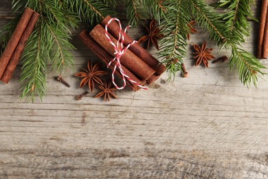 Different spices and fir branches on wooden table, flat lay. Space for text