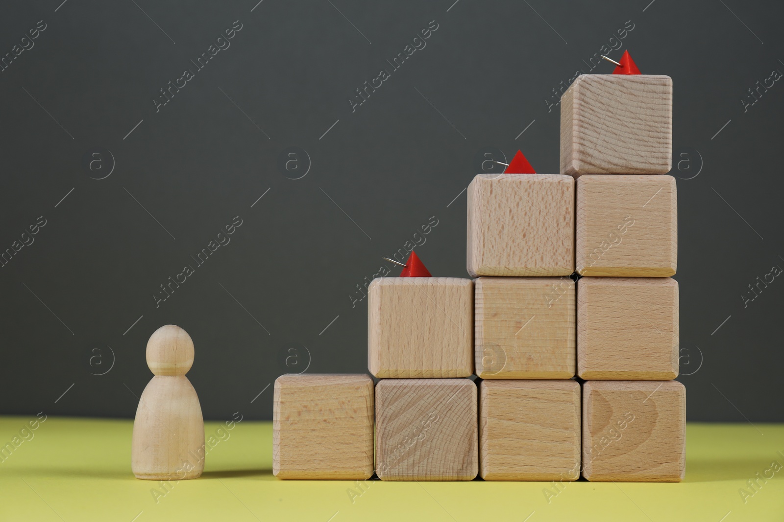 Photo of Stairs of cubes with pins as barrier and wooden human figure on yellow surface, space for text. Path to growth and success