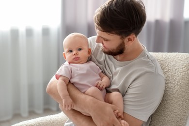 Father with his cute baby in armchair at home, space for text