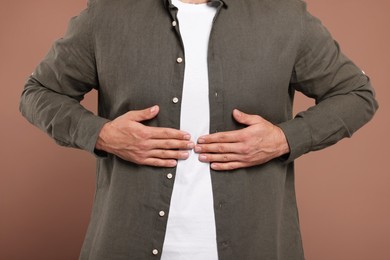 Man suffering from stomach pain on light brown background, closeup