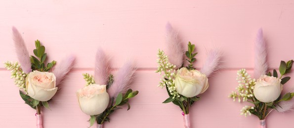 Photo of Many small stylish boutonnieres on pink wooden table, flat lay. Banner design