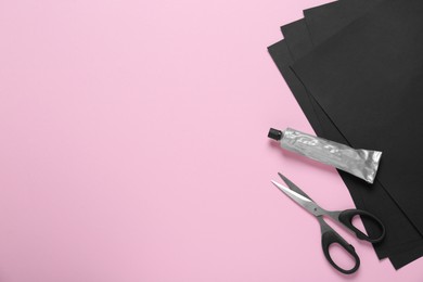 Photo of Tubeglue, black paper and scissors on pink background, flat lay. Space for text