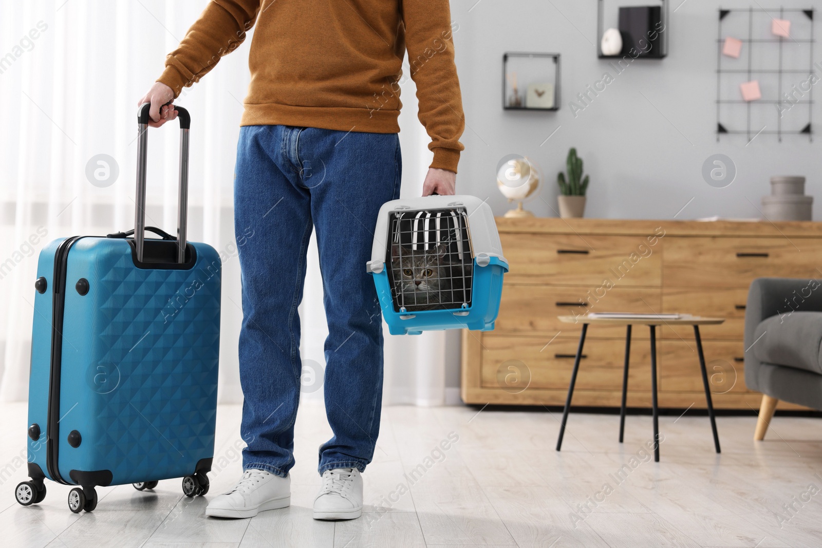 Photo of Travel with pet. Man holding carrier with cute cat and suitcase at home, closeup. Space for text