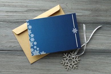 Blank Christmas invitation card, envelope and decorative snowflake on grey wooden table, flat lay