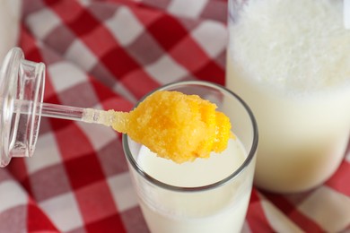 Putting spoon with tasty honey into glass of milk on checkered cloth, closeup