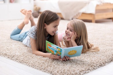 Cute little sisters reading book together at home