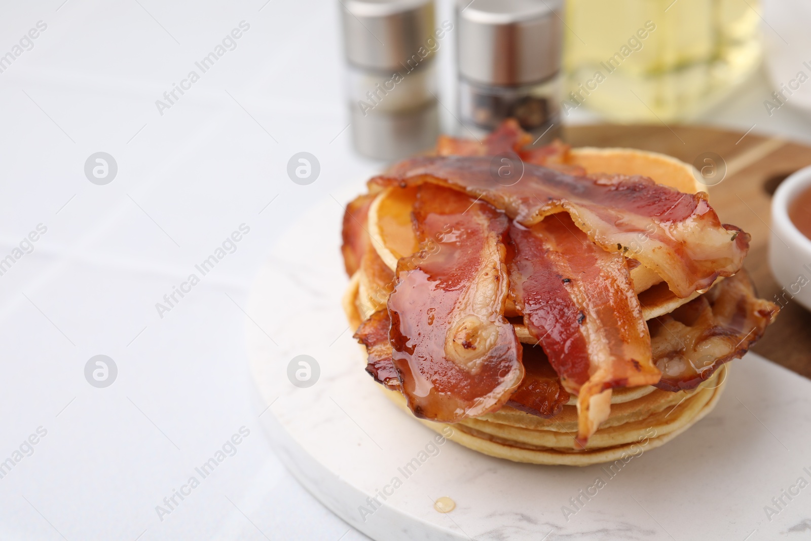 Photo of Delicious pancakes with bacon and honey on white table, closeup. Space for text