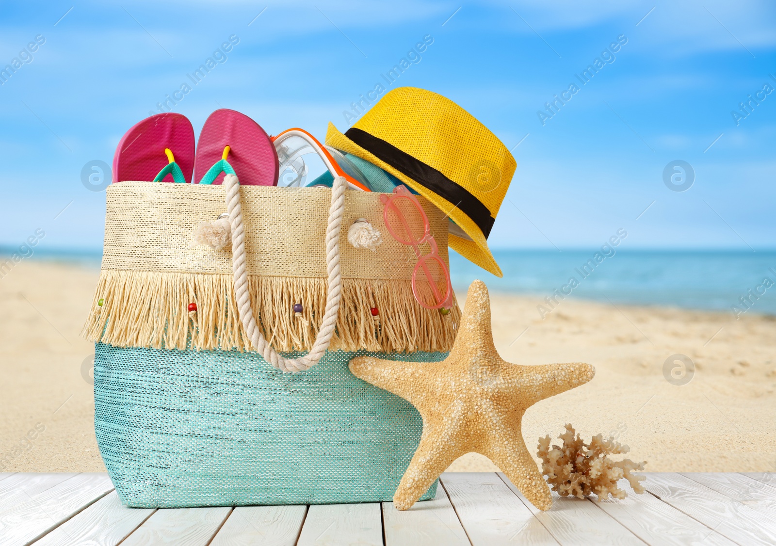 Image of Stylish bag with beach accessories on wooden surface near seashore 