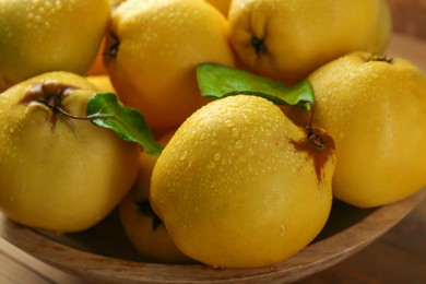 Tasty ripe quince fruits with water drops in wooden bowl on table, closeup