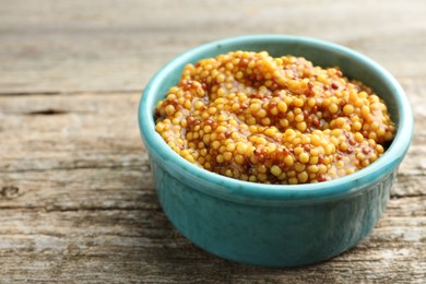 Fresh whole grain mustard in bowl on wooden table, closeup. Space for text