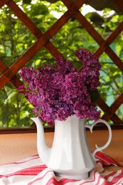 Beautiful lilac flowers in teapot near window indoors