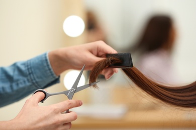 Barber making stylish haircut with professional scissors in beauty salon, closeup