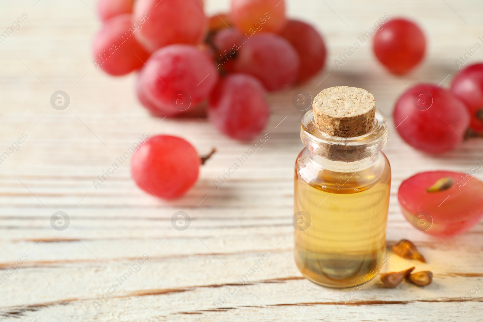 Photo of Organic red grapes, seeds and bottle of natural essential oil on white wooden table. Space for text