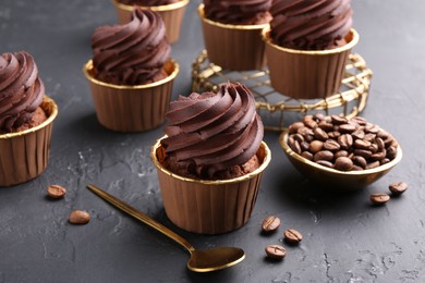 Photo of Delicious chocolate cupcakes and coffee beans on black textured table