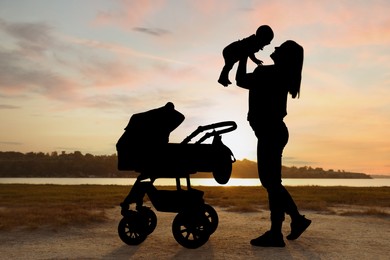 Image of Mother with baby walking outdoors at sunset, silhouette