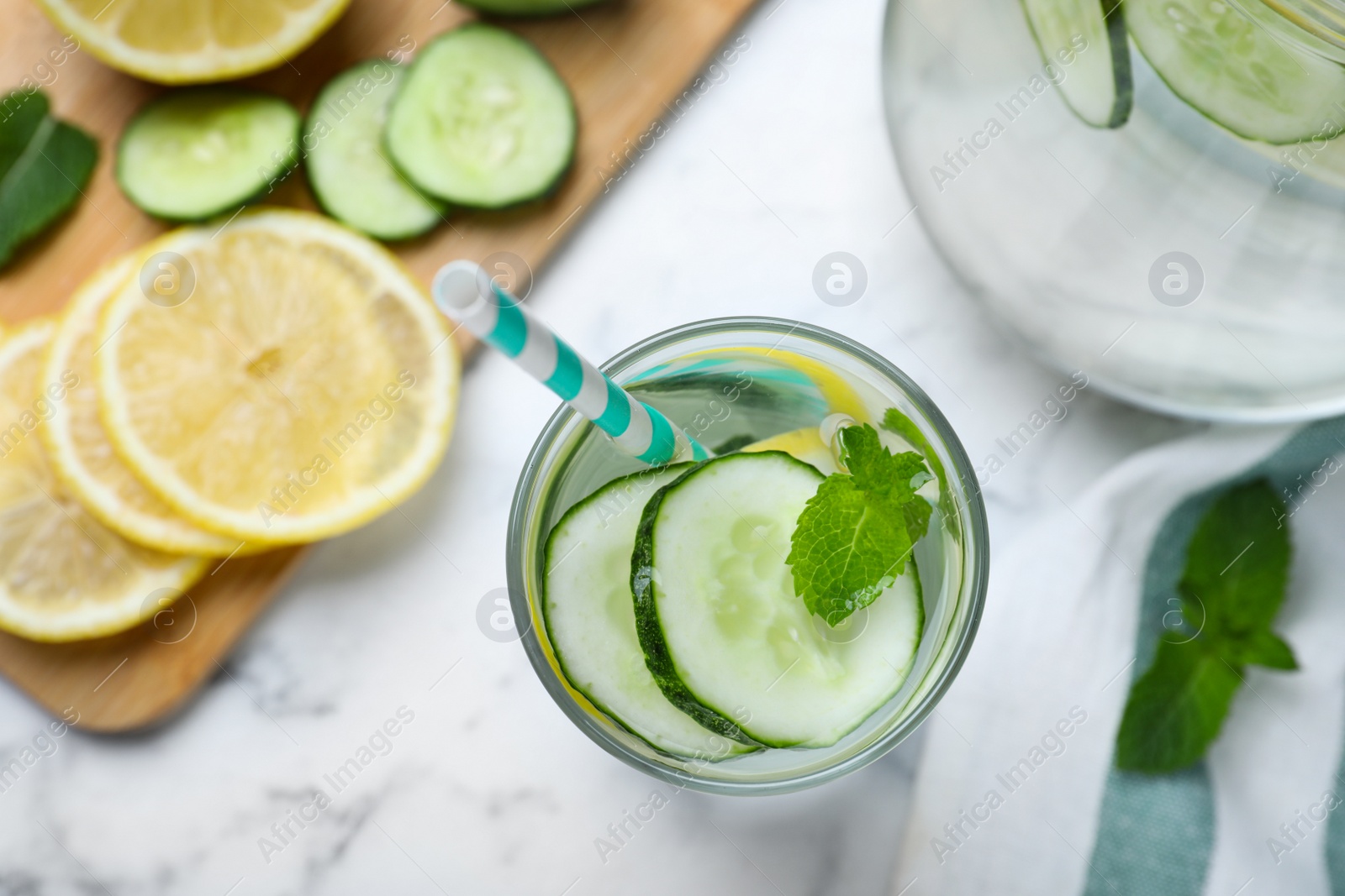 Photo of Refreshing water with cucumber, lemon and mint on white marble table, flat lay