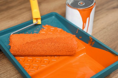 Can of orange paint, tray and roller on wooden table, closeup