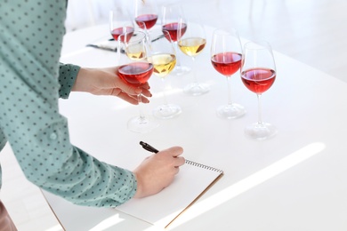 Photo of Woman with notebook tasting delicious wine at table indoors