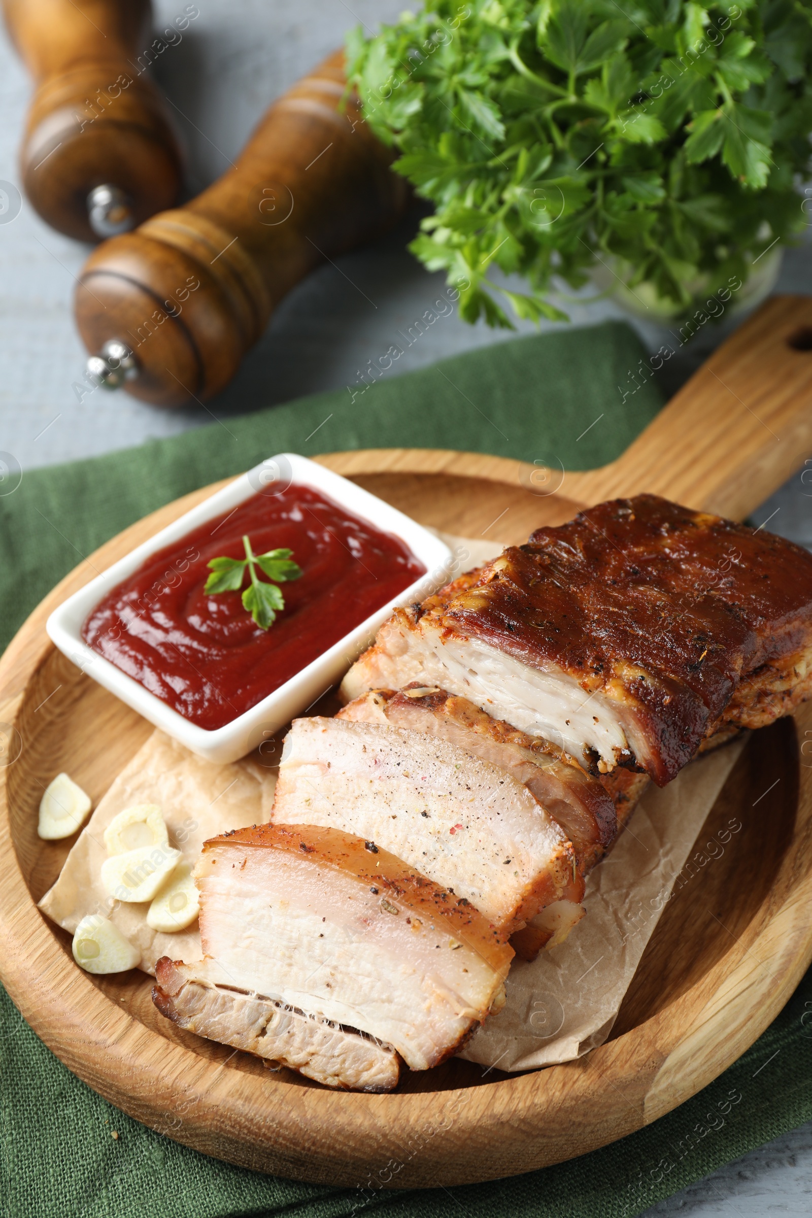 Photo of Pieces of baked pork belly served with sauce on grey wooden table