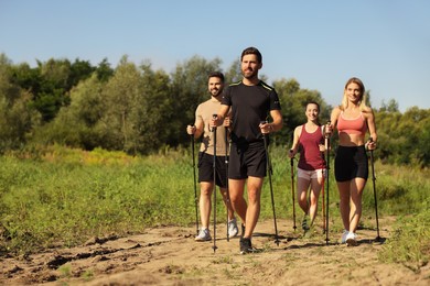 Photo of Group of people practicing Nordic walking with poles outdoors on sunny day