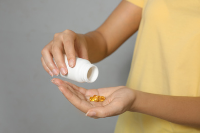Photo of African-American woman with bottle of vitamin capsules on light grey background, closeup