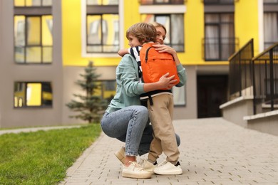 Photo of Happy woman hugging with her son near kindergarten outdoors, low angle view