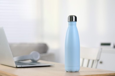 Stylish thermo bottle and laptop on wooden table at home. Space for text