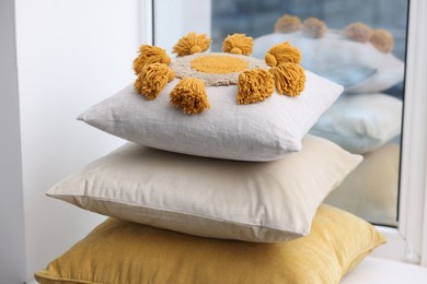 Stack of soft pillows on window sill indoors