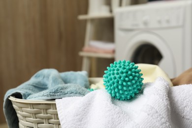 Photo of Turquoise dryer ball and towels in wicker basket near washing machine, closeup. Space for text