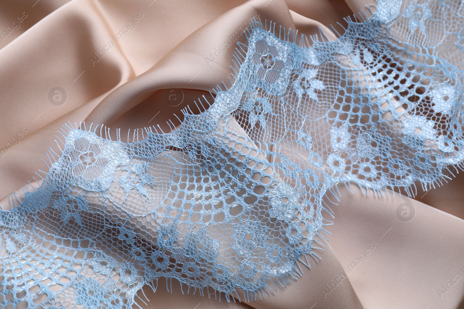 Photo of Beautiful light blue lace on beige fabric, top view