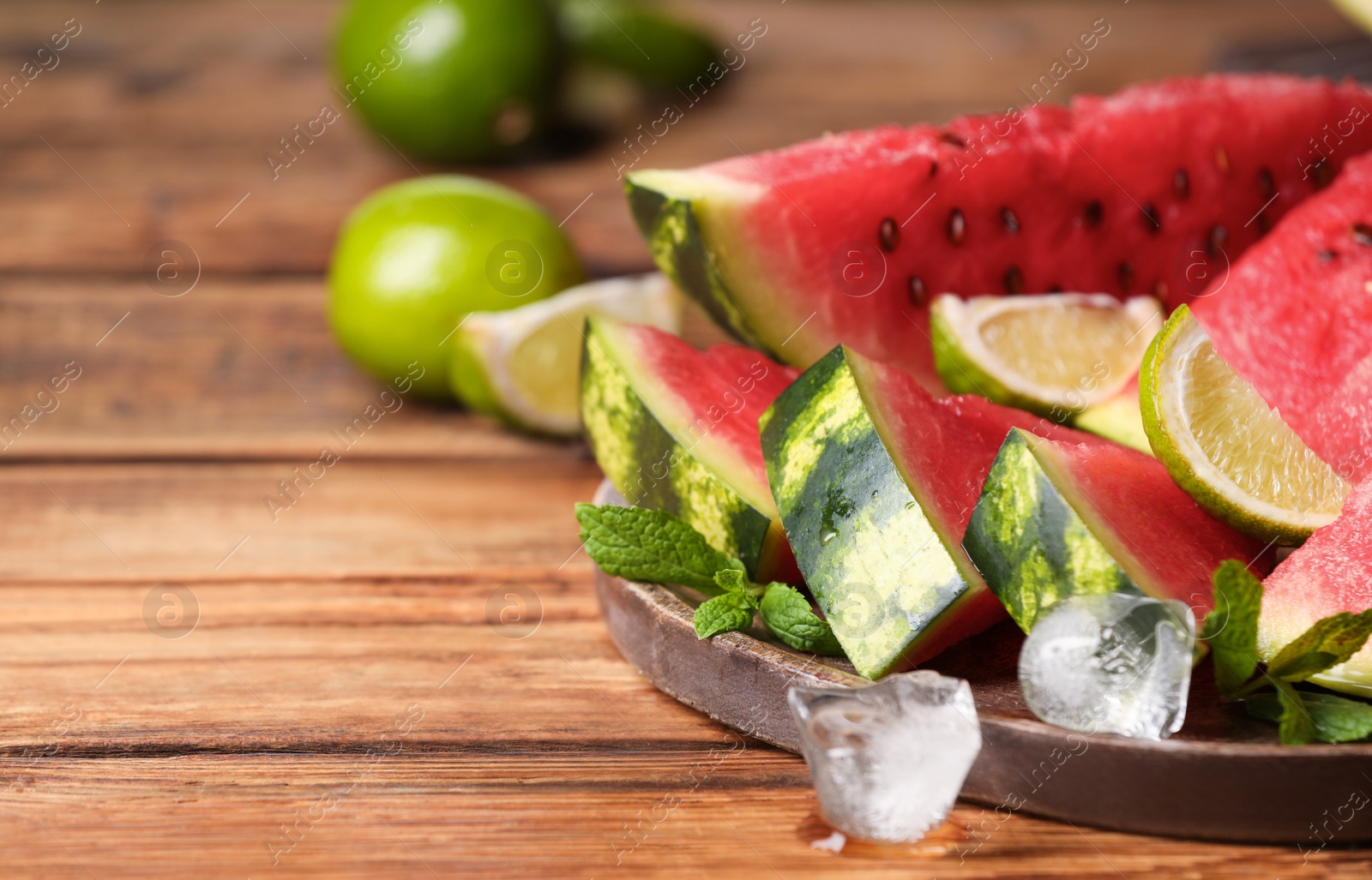 Photo of Slices of delicious ripe watermelon, ice cubes and cut lime on wooden table, closeup. Space for text