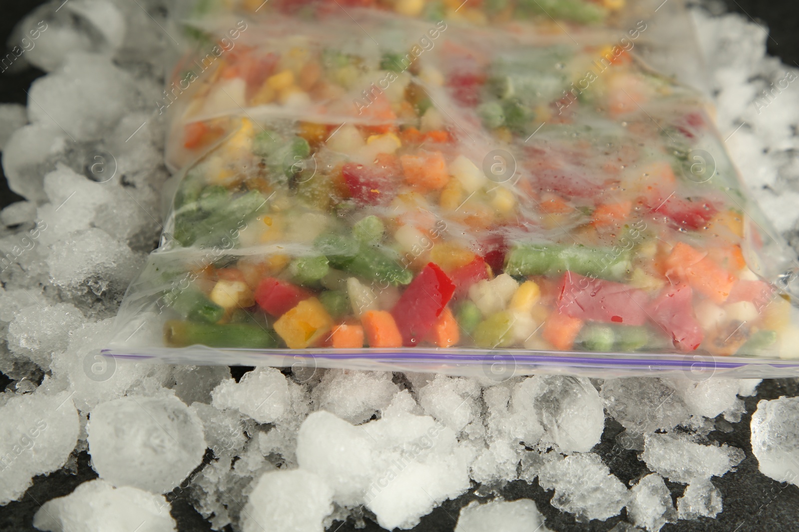 Photo of Zip bag with different frozen vegetables and ice on table, closeup