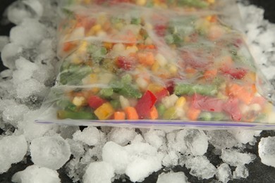 Zip bag with different frozen vegetables and ice on table, closeup