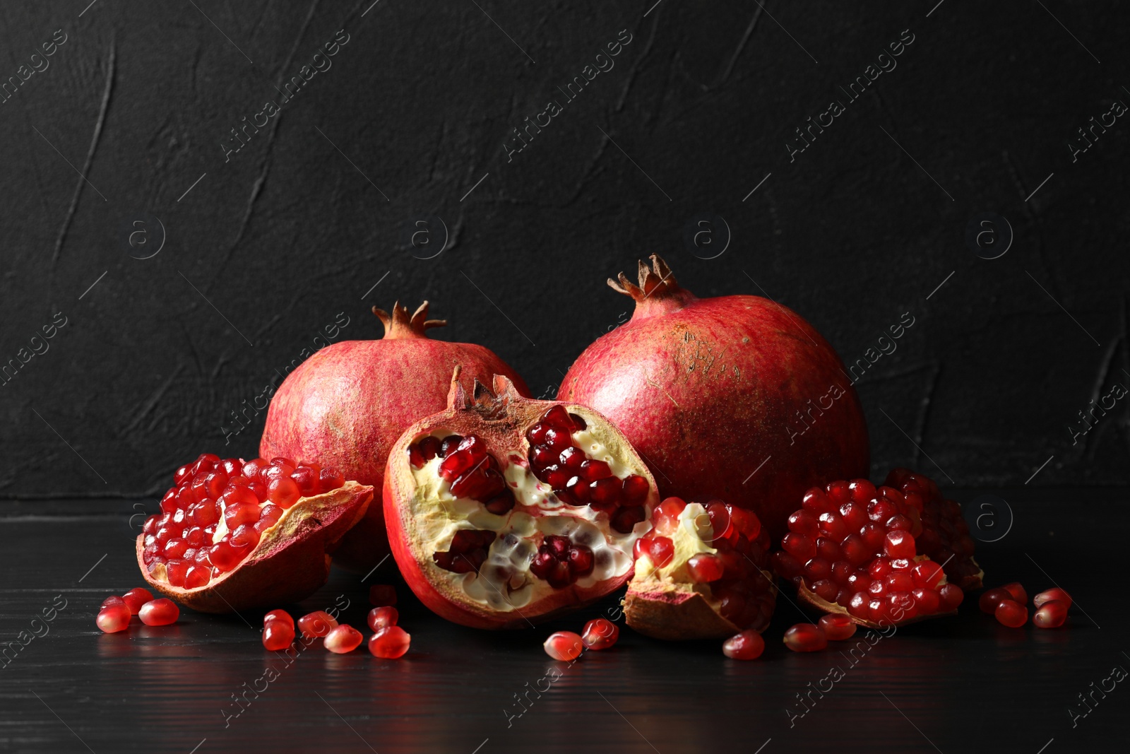 Photo of Ripe pomegranates on table against dark background. Space for text