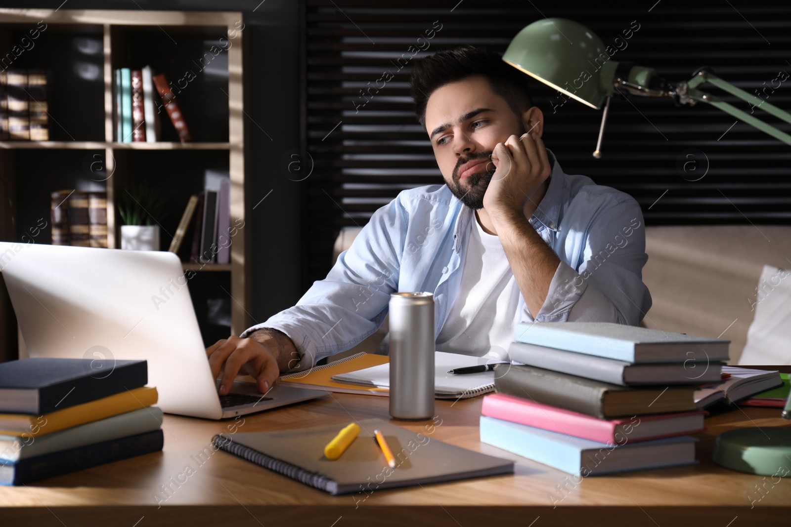 Photo of Tired young man with energy drink studying at home