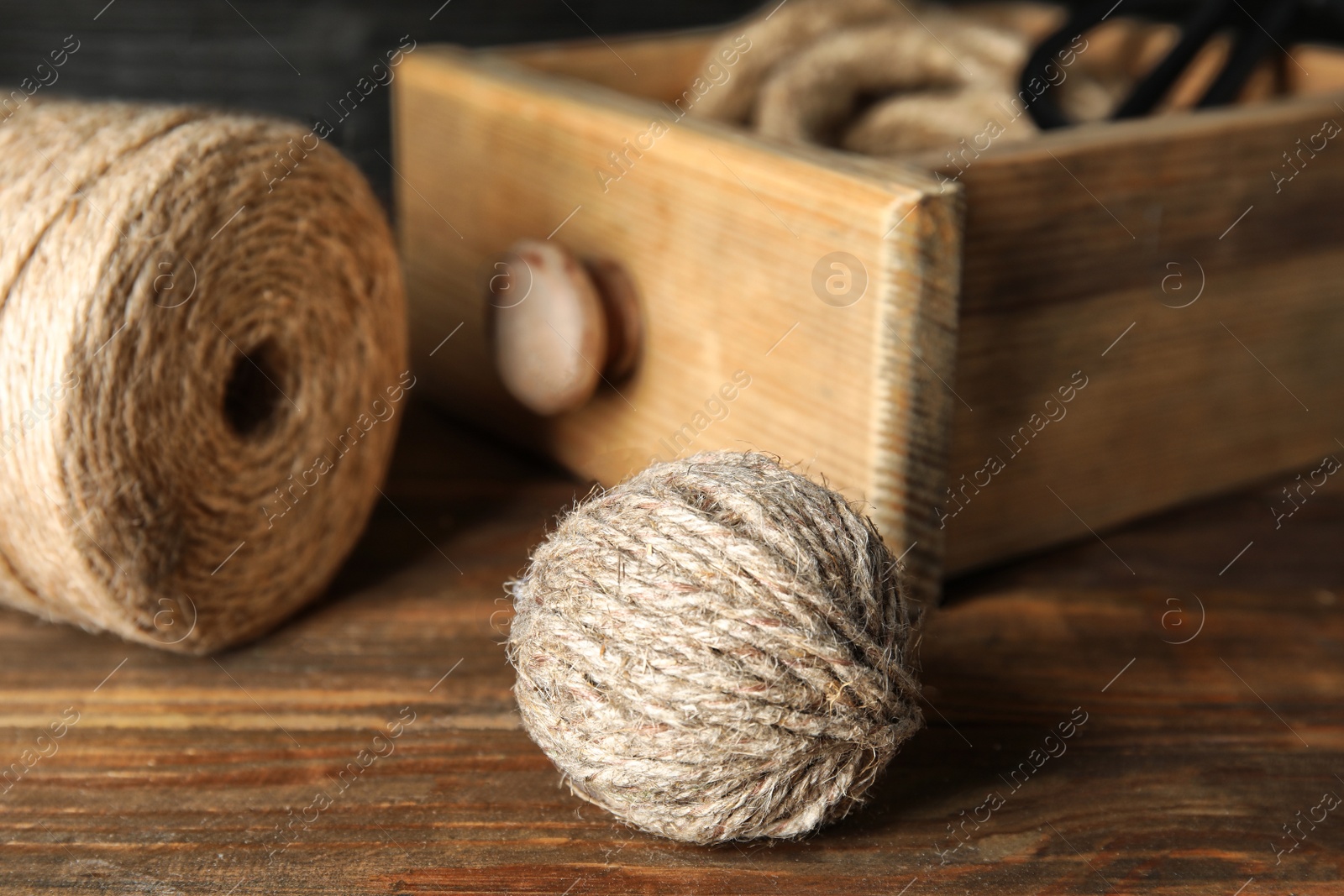 Photo of Ball of natural hemp rope near spool and drawer on wooden table