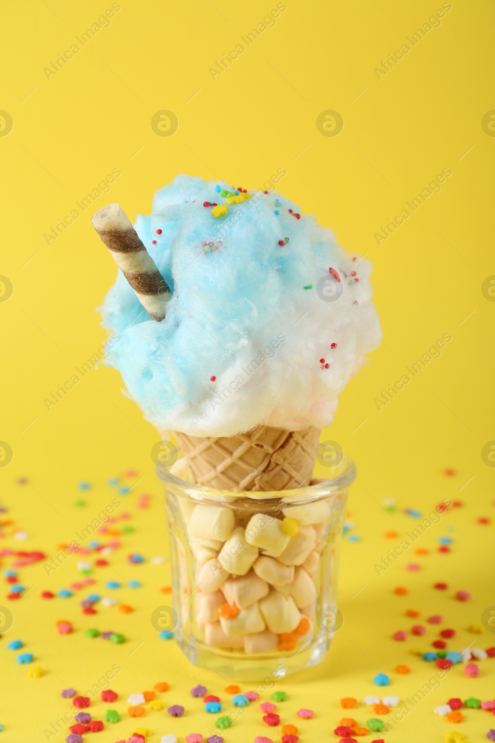 Photo of Sweet cotton candy in waffle cone on yellow background, closeup