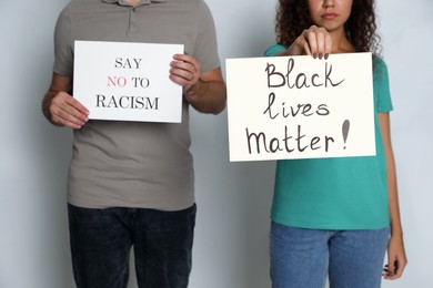Man and African American woman holding signs on grey background, closeup. Racism concept